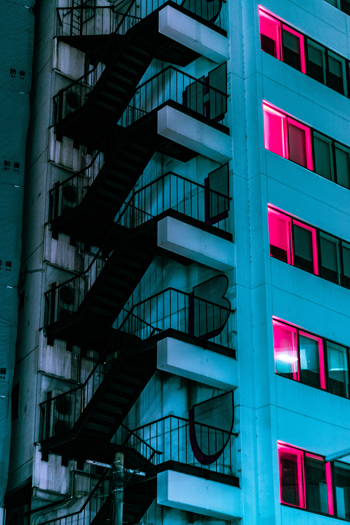 Outdoor stairway with windows on the other side of the building glowing red.
